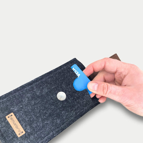 Hand, die eine blaue Karte hält, während sie eine stilvolle dunkle Filztasche für das Handy mit einer Münze darin verwendet.