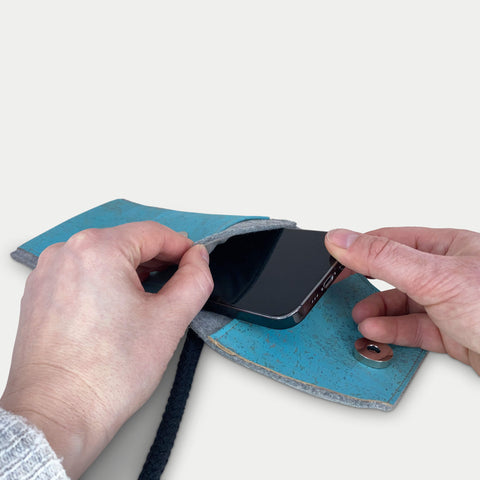 Person, die ein Motorola Moto E15 in eine stilvolle hellgraue und blaue Filztasche mit Schulterriemen steckt.