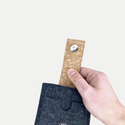 Hand, die eine graue Filzhülle für ein Smartphone mit Korkgriff und Druckknopfverschluss hält, speziell für das Motorola Moto G15 entwickelt.