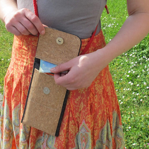 Person, die eine Kork-Handytasche mit Kartenfächern im Freien hält und einen orangefarbenen gemusterten Rock trägt.