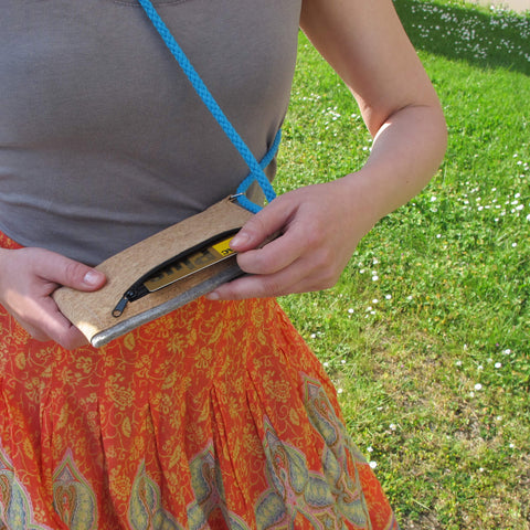 Frau, die eine hellgraue Filztasche mit einem blauen verstellbaren Riemen hält und auf einer Rasenfläche im Freien sitzt.
